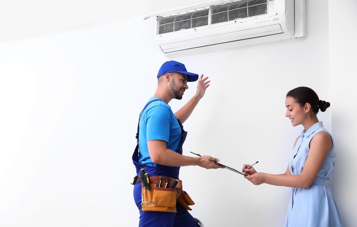 Técnico refrigerista com cinto de ferramentas explica contrato de manutenção de ar-condicionado para cliente