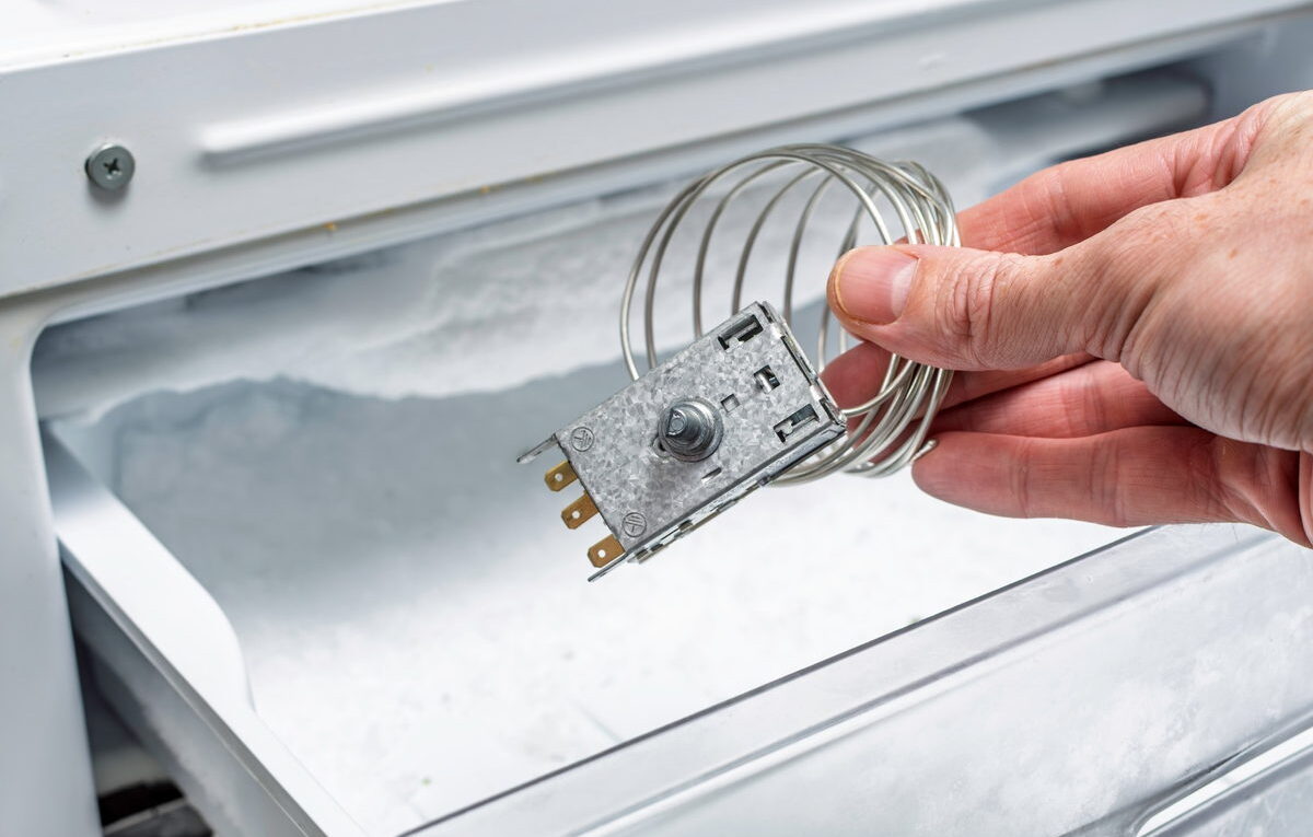Mão retirando termostato de freezer com defeito de dentro do congelador para realizar teste de continuidade