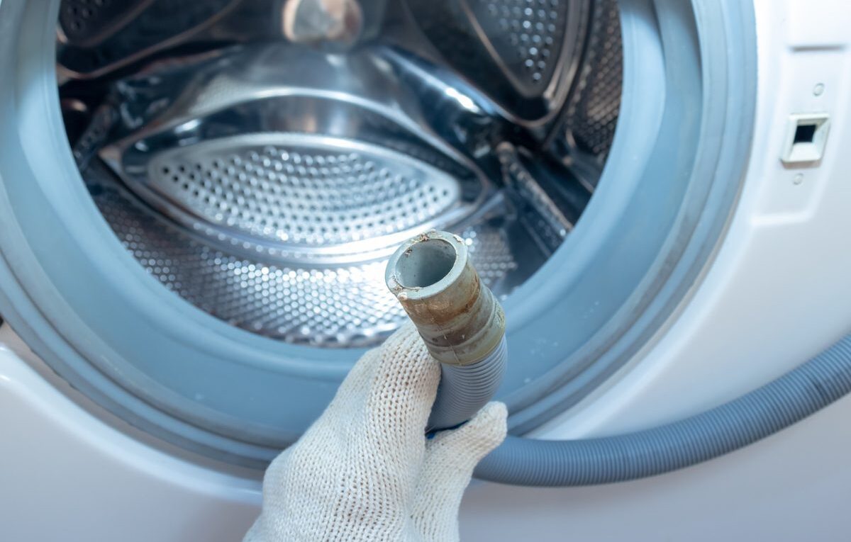 Técnico segurando mangueira de máquina de lavar durante inspeção de vazamento na lavadora.