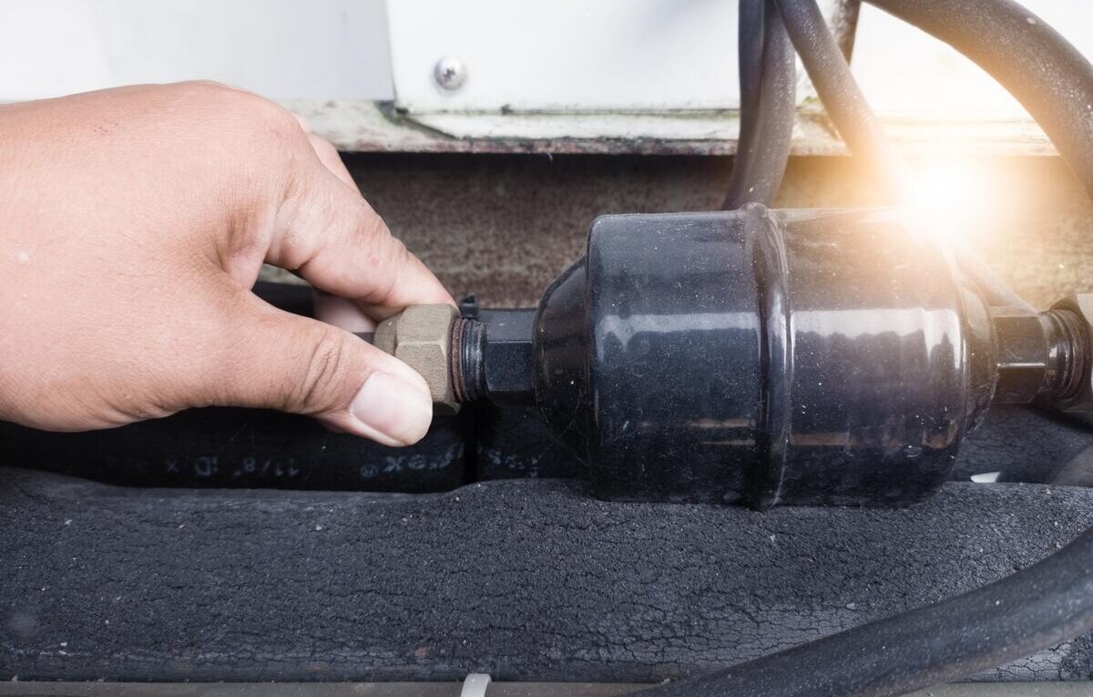 Técnico manuseia filtro secador conectado à tubulação de um sistema de refrigeração.