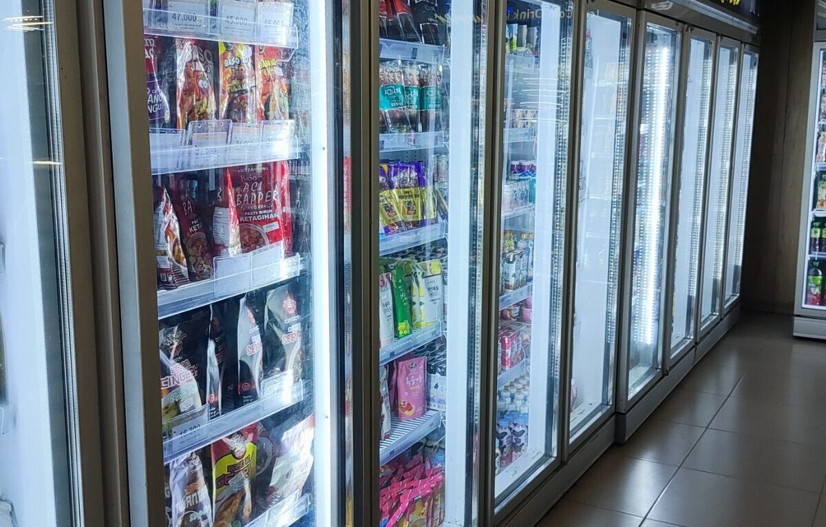 Fileira de refrigeradores expositores verticais com portas de vidro em um estabelecimento comercial