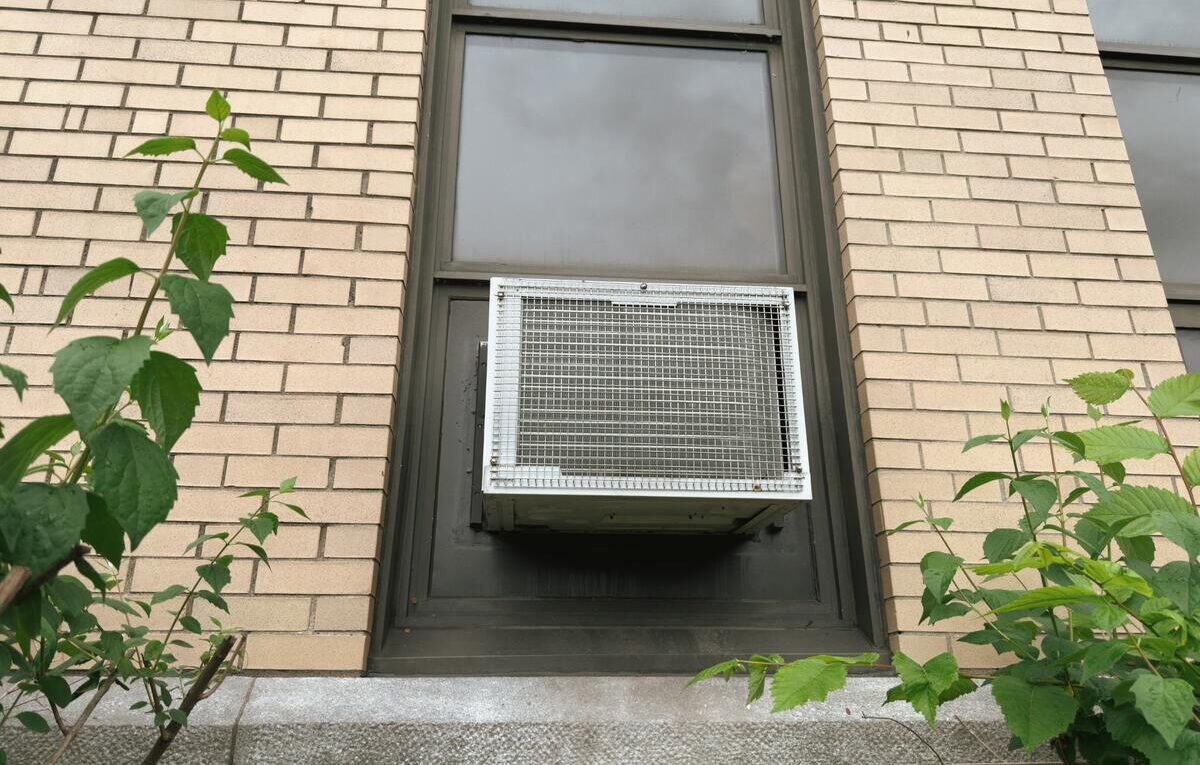 Ar-condicionado de janela instalado em uma fachada, visto pelo lado externo, com a grade traseira do sistema de ventilação.