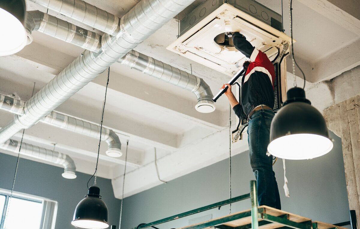 Técnico faz manutenção em ar-condicionado cassete instalado no teto de um espaço comercial.