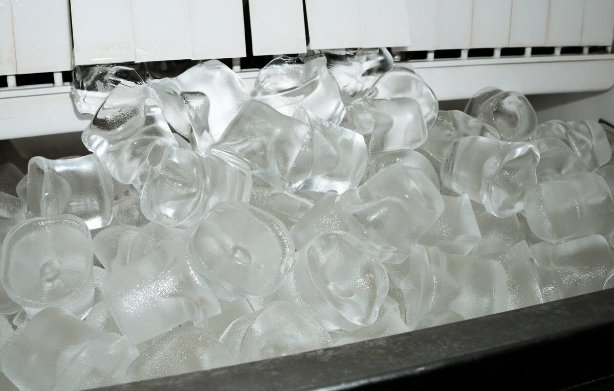 Cubos de gelo transparentes acumulados abaixo do mecanismo de produção de uma máquina de gelo.
