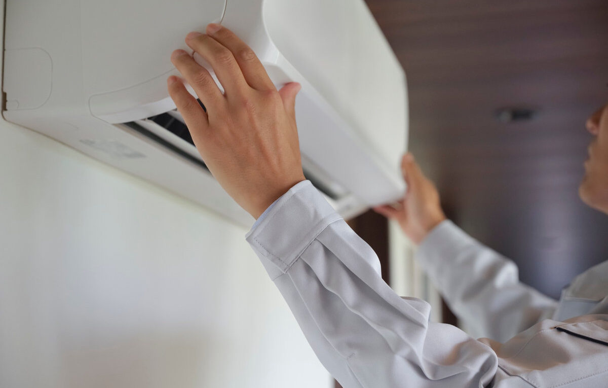 Profissional manuseando a unidade interna de um ar-condicionado split branco instalado na parede.