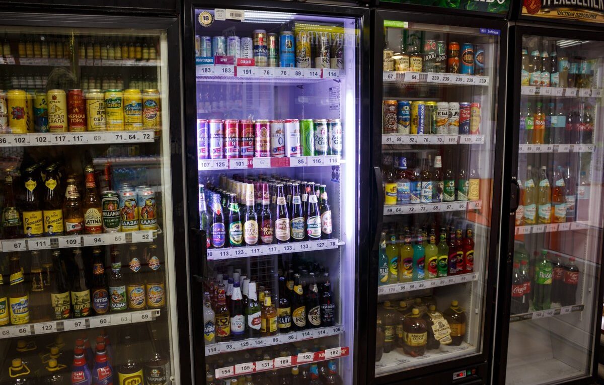Cervejeiras expositoras com portas de vidro e prateleiras abastecidas com latas e garrafas de bebidas.